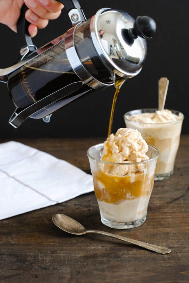 Two small glasses of ice cream, with a person pouring coffee from a French press over the ice cream.