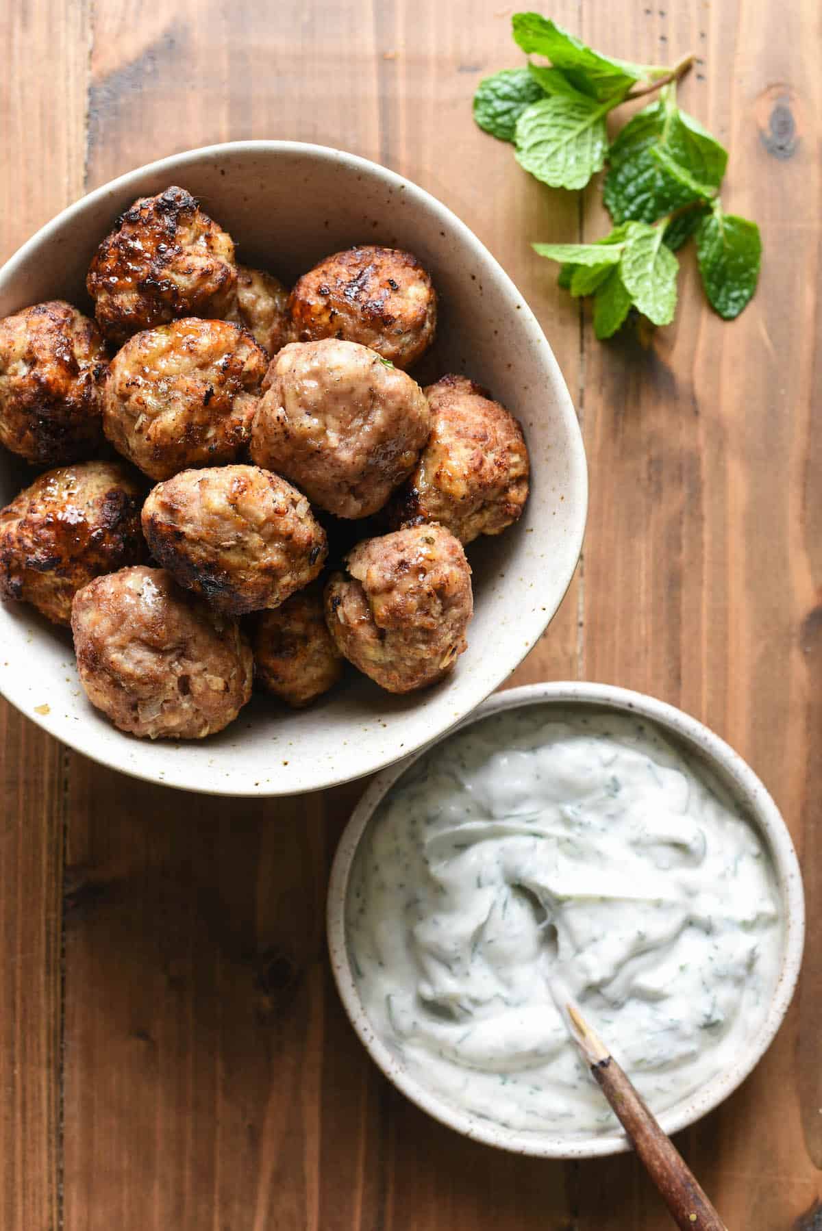 Are you looking for a turkey meatball that isn't dry? These Air Fryer Turkey Meatballs are for you! Cook in an air fryer or oven, and they turn out juicy and flavorful every time. | foxeslovelemons.com A bowl of turkey meatballs air fryer and a bowl of herbed yogurt sauce, with a mint sprig.