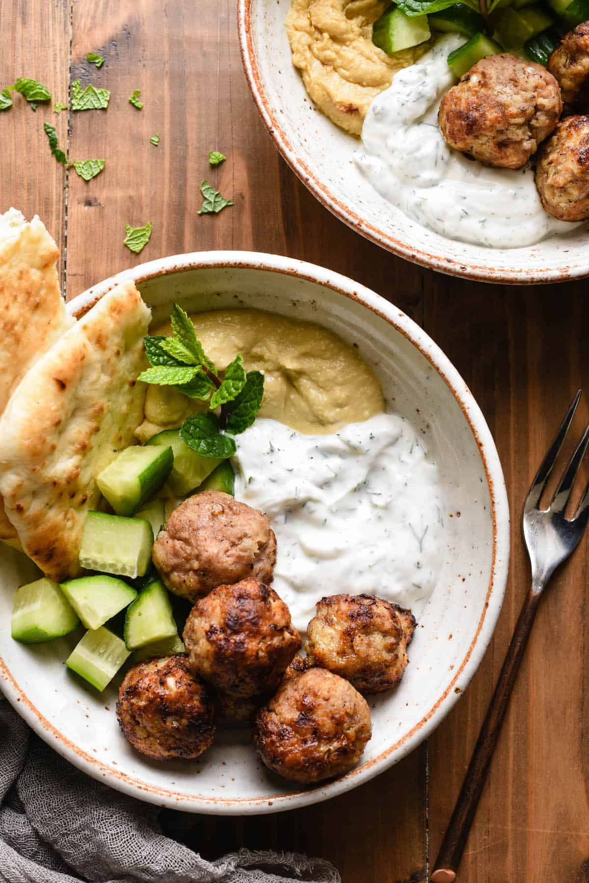 Are you looking for a turkey meatball that isn't dry? These Air Fryer Turkey Meatballs are for you! Cook in an air fryer or oven, and they turn out juicy and flavorful every time. | foxeslovelemons.com Two bowls filled with turkey meatballs in air fryer, diced cucumbers, herbed yogurt sauce, hummus and naan bread.