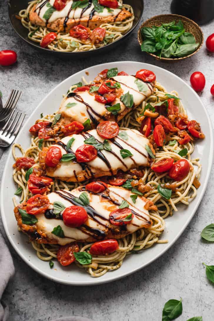 A white platter topped with baked chicken caprese over pesto spaghetti.