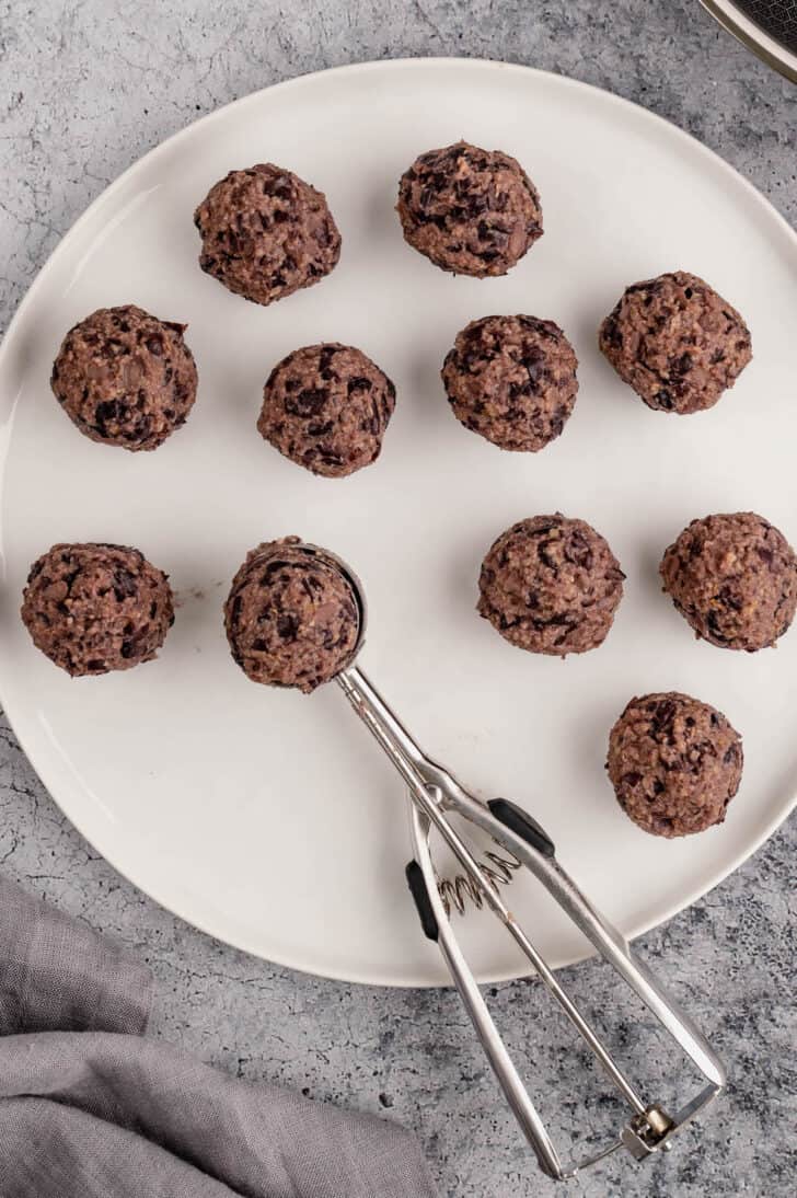 Uncooked black bean meatballs on a white plate, after being formed by a small cookie scoop.