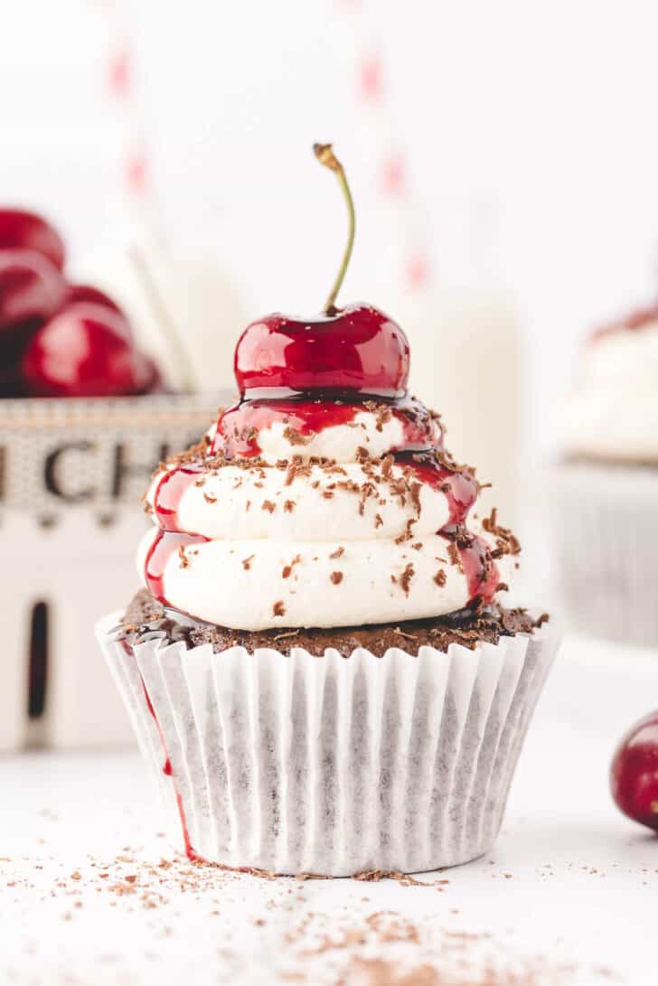 A Black Forest cupcake topped with whipped cream, chocolate shavings and a cherry.