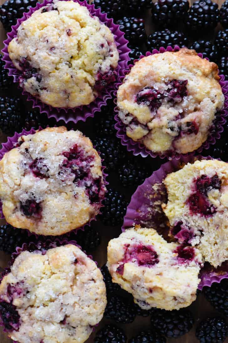 Five fruit quick breads in purple paper liners on a bed of berries, with one bread split in half.