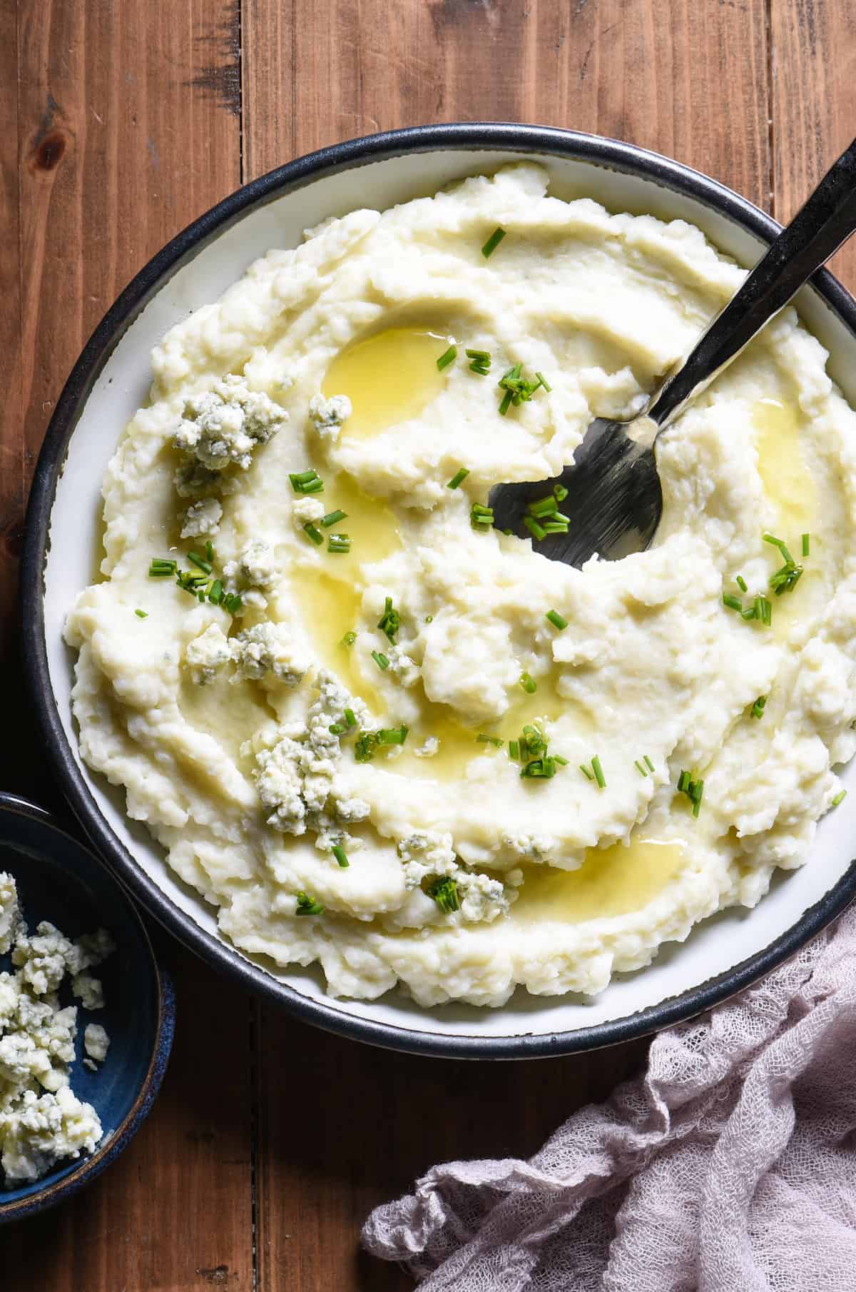 These creamy Blue Cheese Mashed Potatoes are a tangy twist on a classic. They're the perfect pairing for prime rib, ham or even turkey! | foxeslovelemons.com A shallow bowl filled with blue cheese mashed potatoes garnished with melted butter and chives.