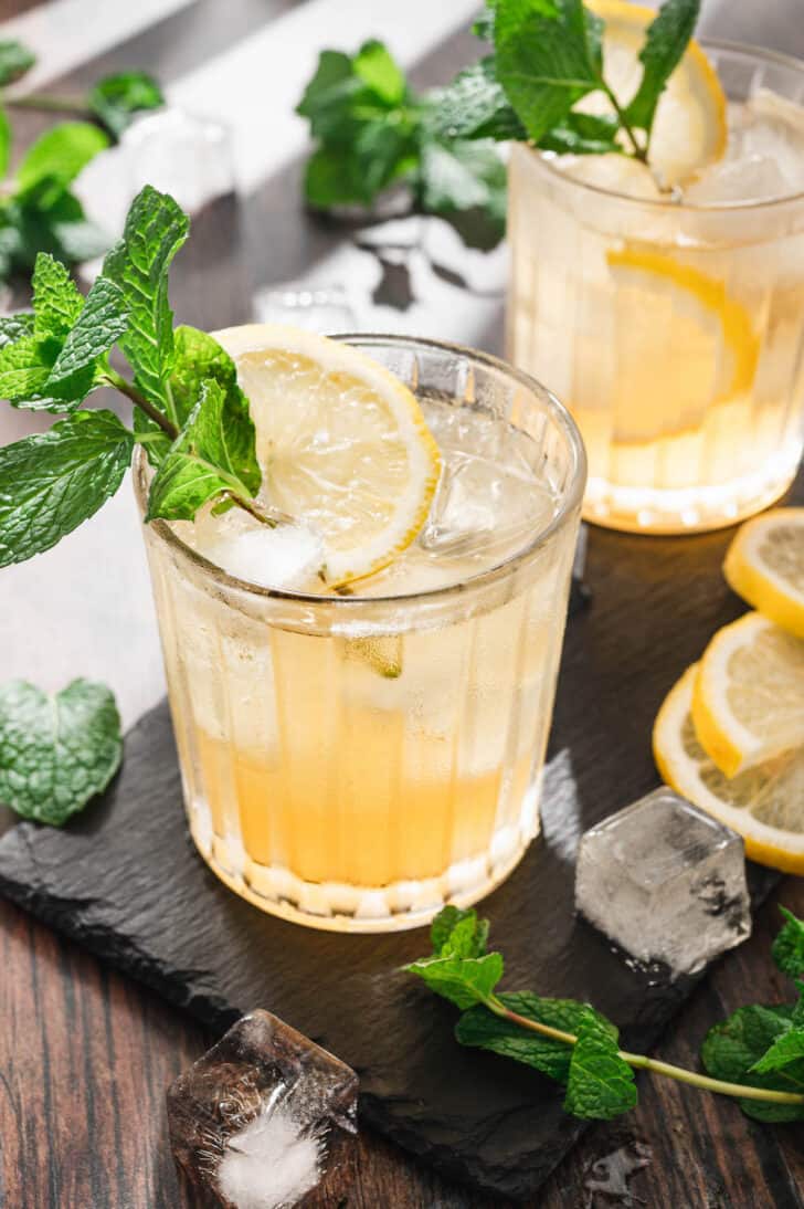 A yellow-hued cocktail garnished with a mint sprig and lemon slice.