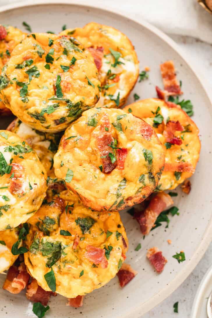 A white plate topped with breakfast muffins made with eggs, bacon, veggies, cheese and herbs.