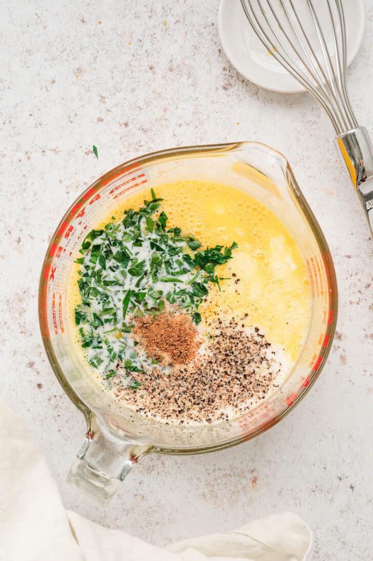 A large glass measuring cup with a yellow liquid topped with herbs and spices.