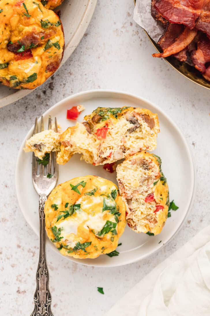 Two egg muffin cups on a white plate, with one of them having been cut in half, exposing the veggies inside.