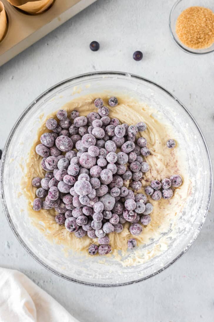 A glass bowl filled with yellow batter and frozen fruit.