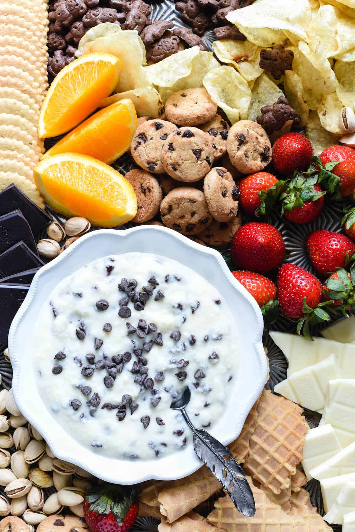 Celebrate every day with this ricotta and mascarpone delight. It's so easy, you can whip it up on a whim. Just five ingredients and five minutes. Serve with sweet and salty dippers of your choice. | foxeslovelemons.com Ricotta and mascarpone mixture topped with mini chocolate chips in fluted white bowl, surrounded by cookies, fruit, chocolate and nuts.