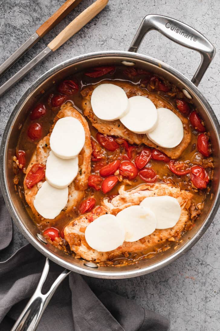 Chicken caprese being made in a stainless steel skillet.