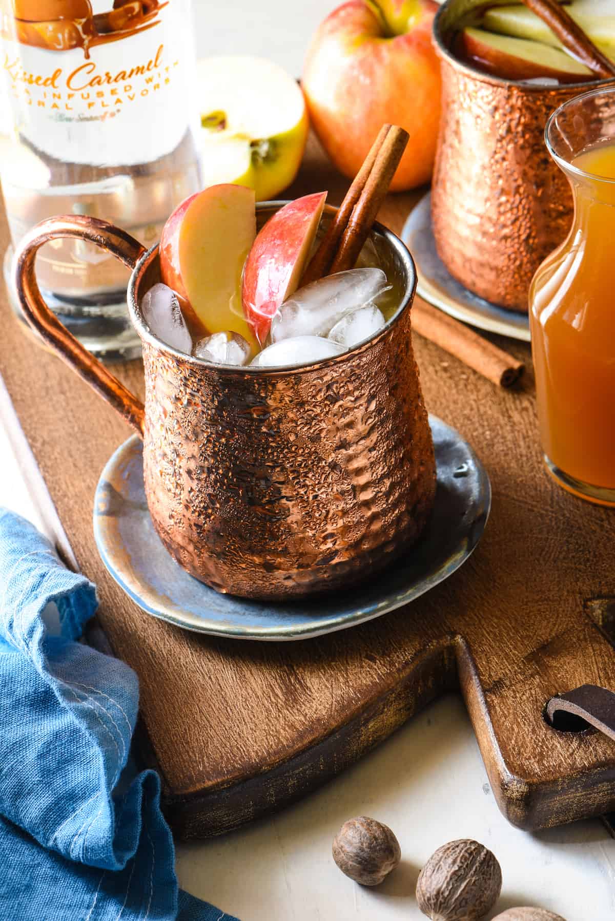 Caramel Apple Pie Moscow Mules - This twist on a classic will take you from summer right into fall. All the best flavors of an apple pie (and caramel!) are added to an ice cold vodka cocktail. | foxeslovelemons.com Copper Moscow mule mug filled with apple cider and vodka, garnished with fresh apple slices and cinnamon sticks.