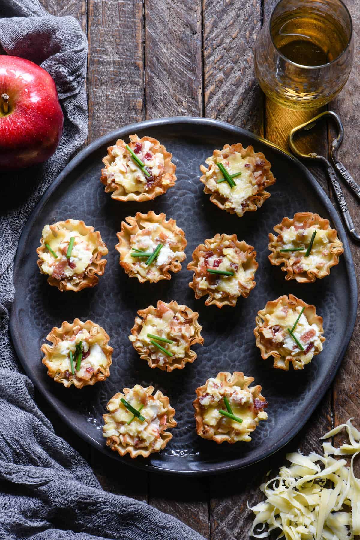 Update your holiday snack spread with these Cheesy Apple & Bacon Phyllo Cup Appetizers - a modern take on a cheeseball and crackers. | foxeslovelemons.com Round gray decorative plate filled with phyllo cup appetizers on a wood table.