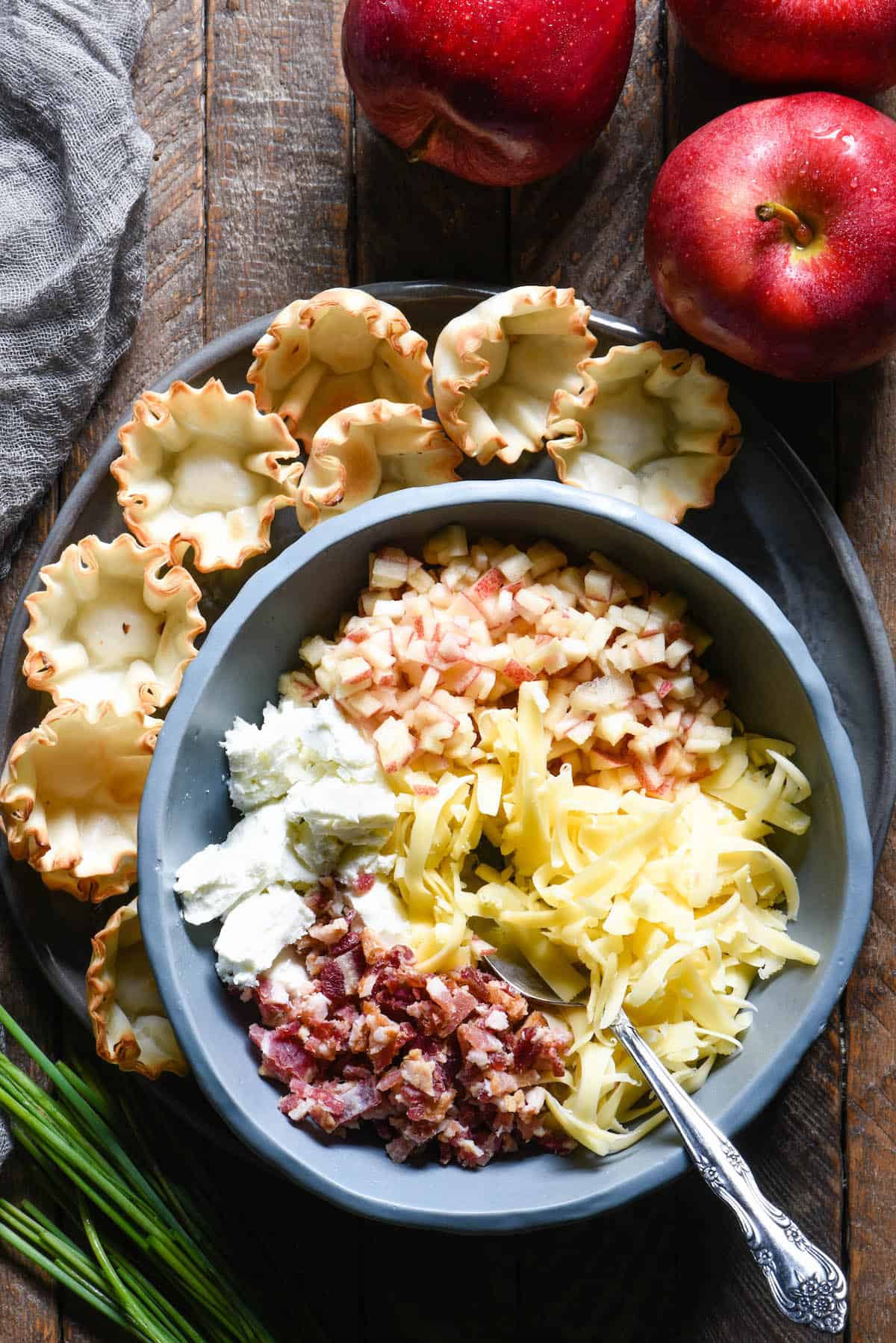 Update your holiday snack spread with these Cheesy Apple & Bacon Phyllo Cup Appetizers - a modern take on a cheeseball and crackers. | foxeslovelemons.com Bowl filled with bacon, goat cheese, light yellow shredded cheese and chopped apples, with empty phyllo cups nearby.
