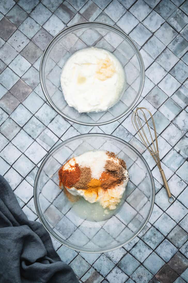 Two glass bowls, one large and one medium, filled with the ingredients needed for chicken shawarma marinade and yogurt sauce.