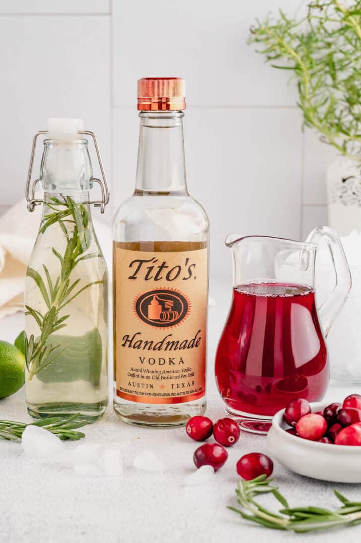 Ingredients needed to make cranberry cocktails, including vodka, cranberry juice and rosemary simple syrup.