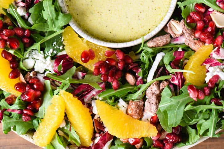 A side dish made with greens, oranges, cheese, pomegranate seeds and nuts.