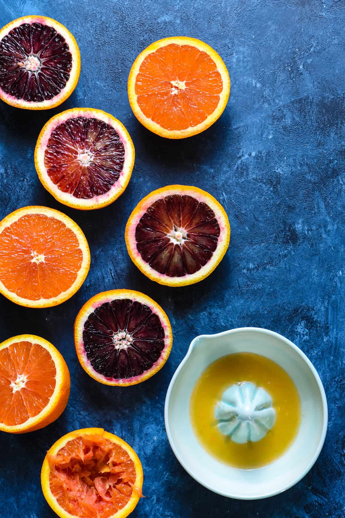 Blood Oranges and Cara Cara Oranges and ceramic juice on blue background.