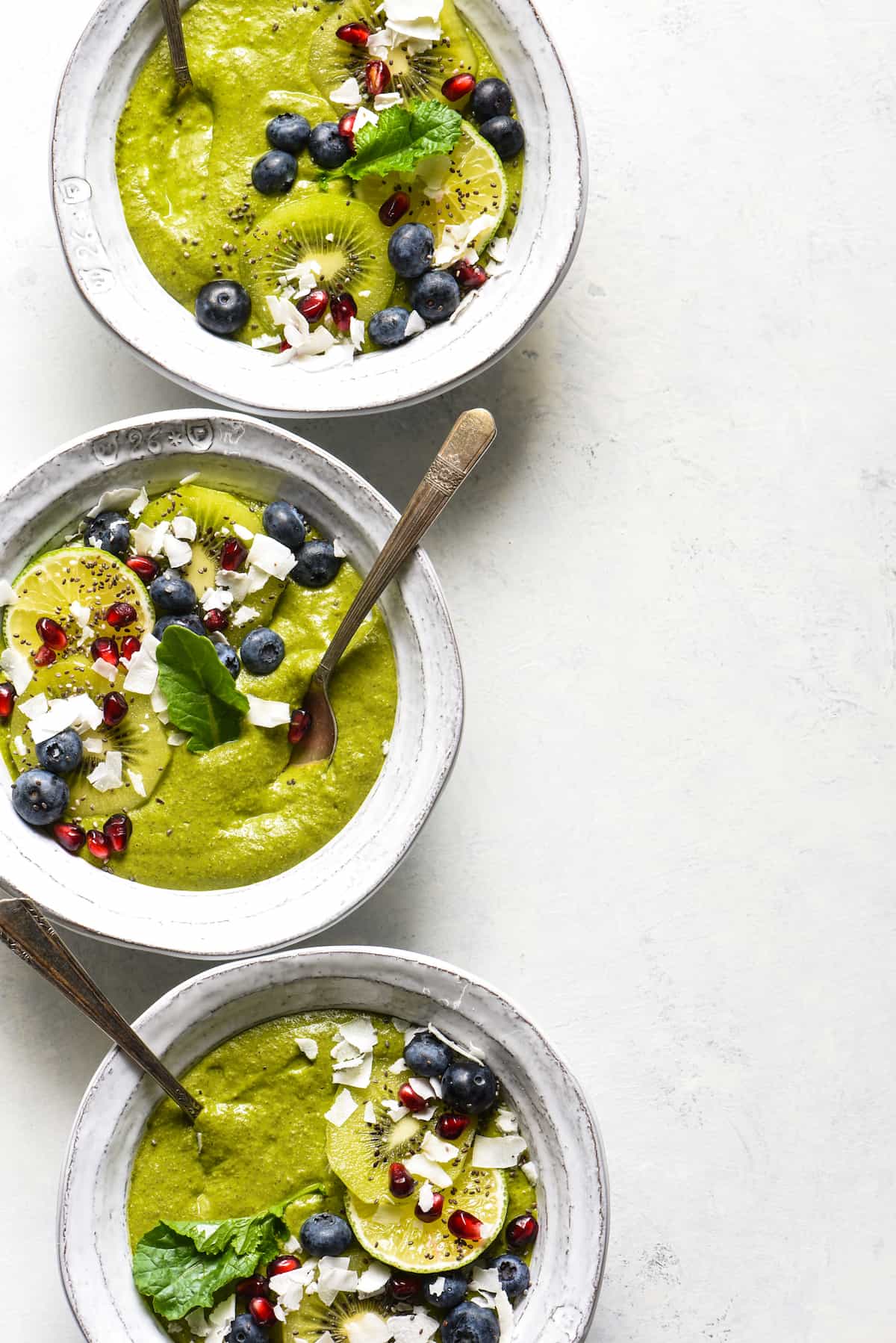 This Citrus Zing Green Smoothie Bowl is a fresh, brightly-flavored green smoothie packed with nutrients and topped with your favorite garnishes! Naturally gluten free, dairy free and vegan. | foxeslovelemons.com Three tropical smoothie bowls topped with blueberries, pomegranate seeds, coconut, kiwi and a green leaf.