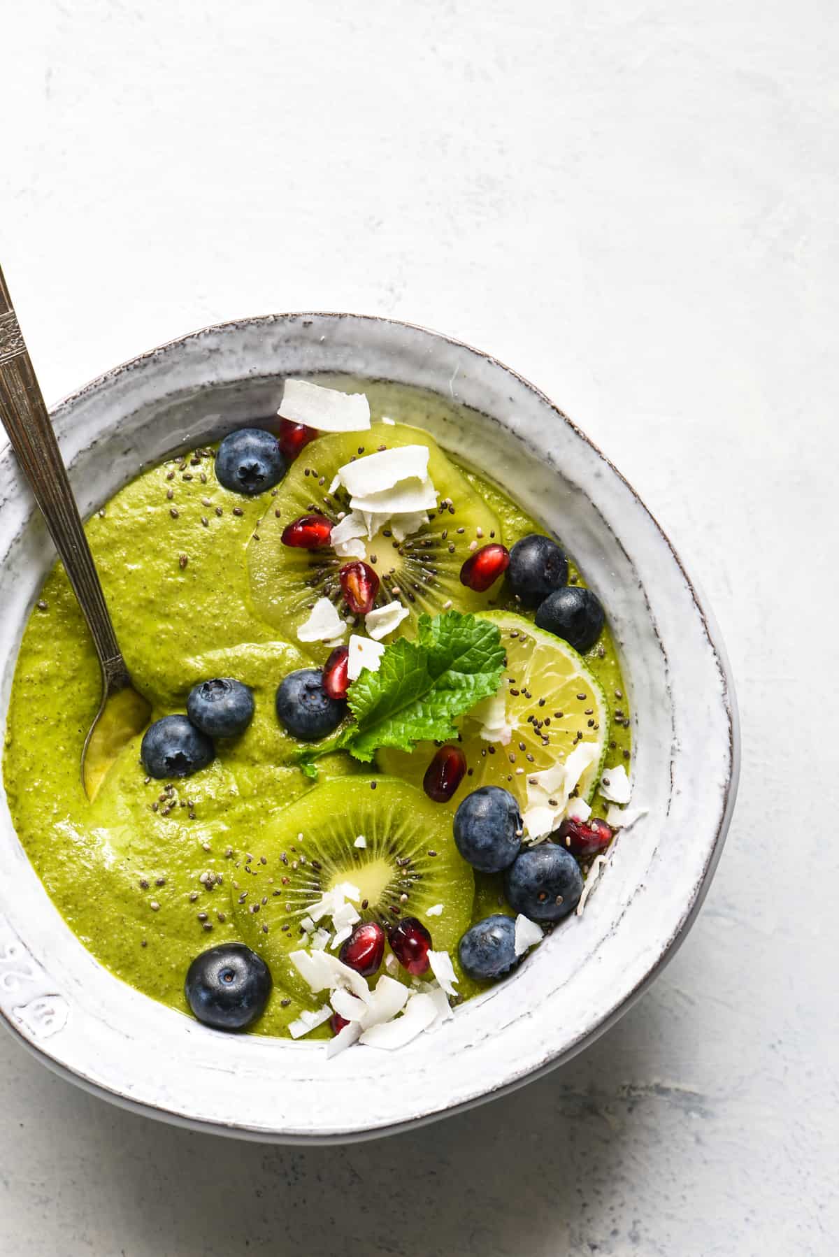 This Citrus Zing Green Smoothie Bowl is a fresh, brightly-flavored green smoothie packed with nutrients and topped with your favorite garnishes! Naturally gluten free, dairy free and vegan. | foxeslovelemons.com A green smoothie bowl topped with blueberries, pomegranate seeds, coconut, kiwi and a green leaf.