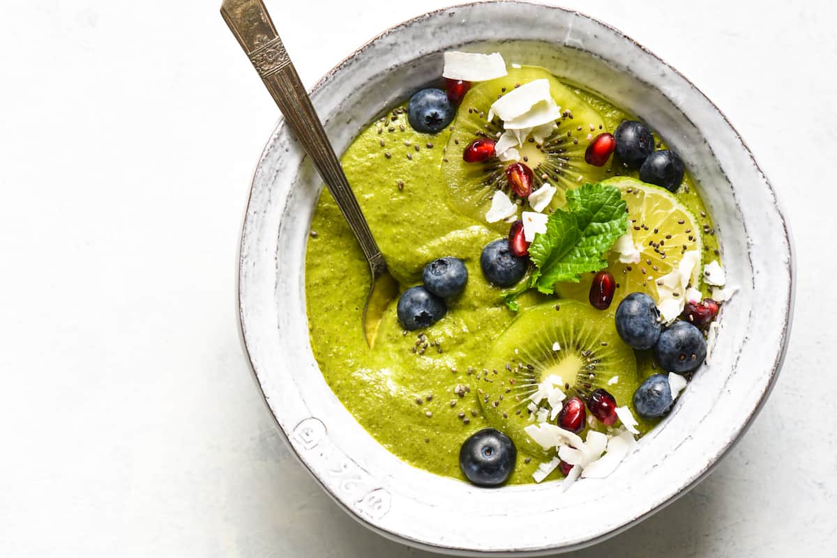 This Citrus Zing Green Smoothie Bowl is a fresh, brightly-flavored green smoothie packed with nutrients and topped with your favorite garnishes! Naturally gluten free, dairy free and vegan. | foxeslovelemons.com A green smoothie bowl topped with blueberries, pomegranate seeds, coconut, kiwi and a green leaf.