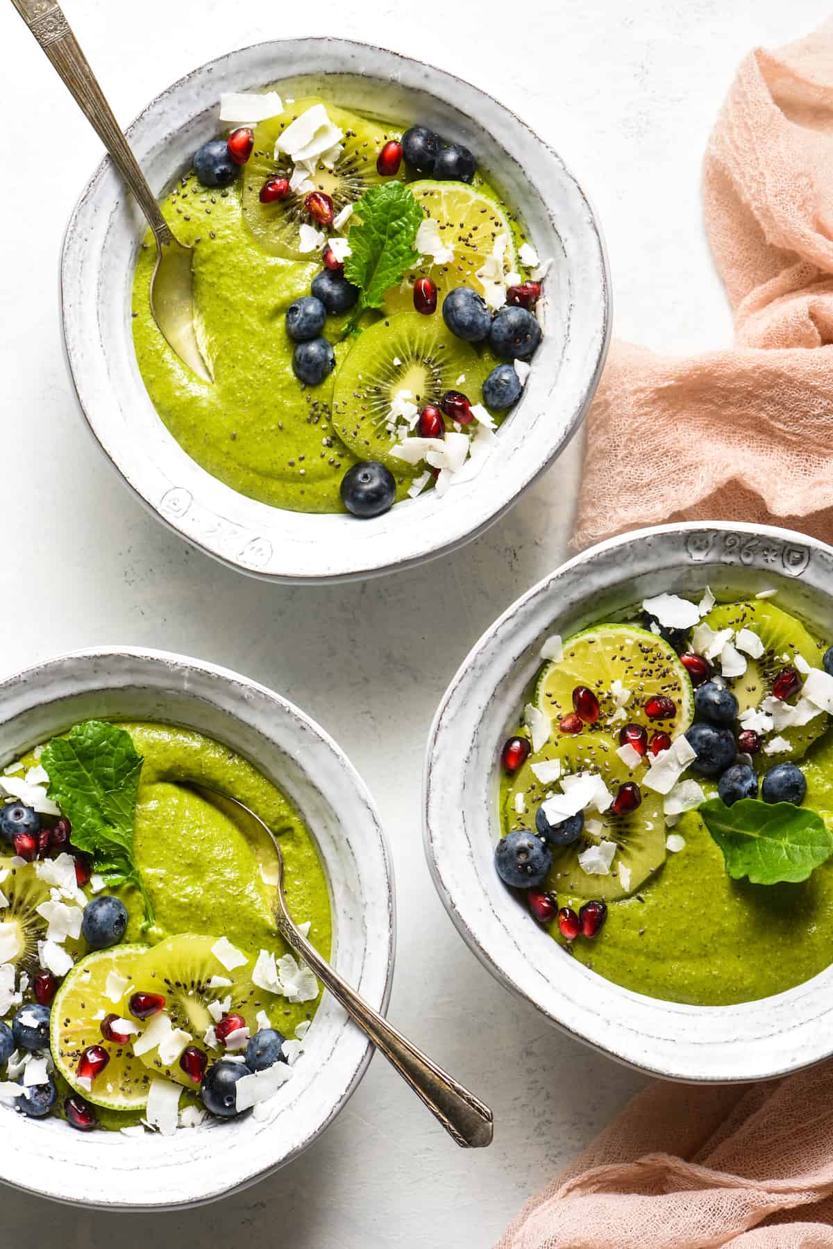This Citrus Zing Green Smoothie Bowl is a fresh, brightly-flavored green smoothie packed with nutrients and topped with your favorite garnishes! Naturally gluten free, dairy free and vegan. | foxeslovelemons.com Three fruit smoothie bowls topped with blueberries, pomegranate seeds, coconut, kiwi and a green leaf.