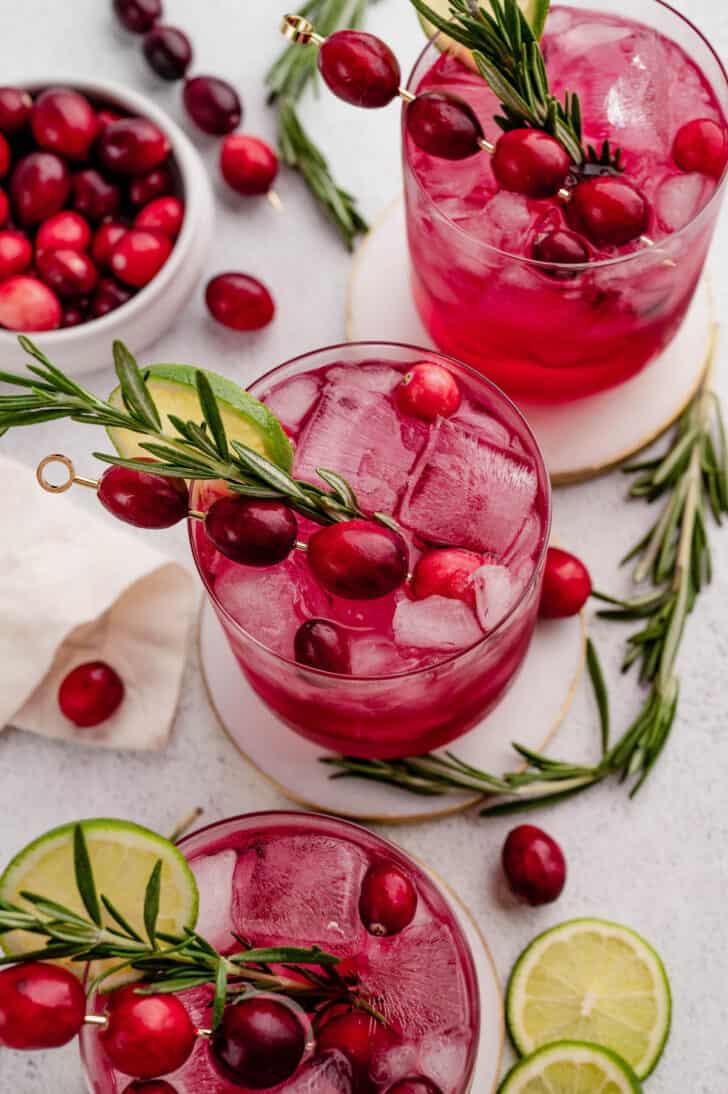 Three red hued drinks garnished with herb sprigs and fresh berries.