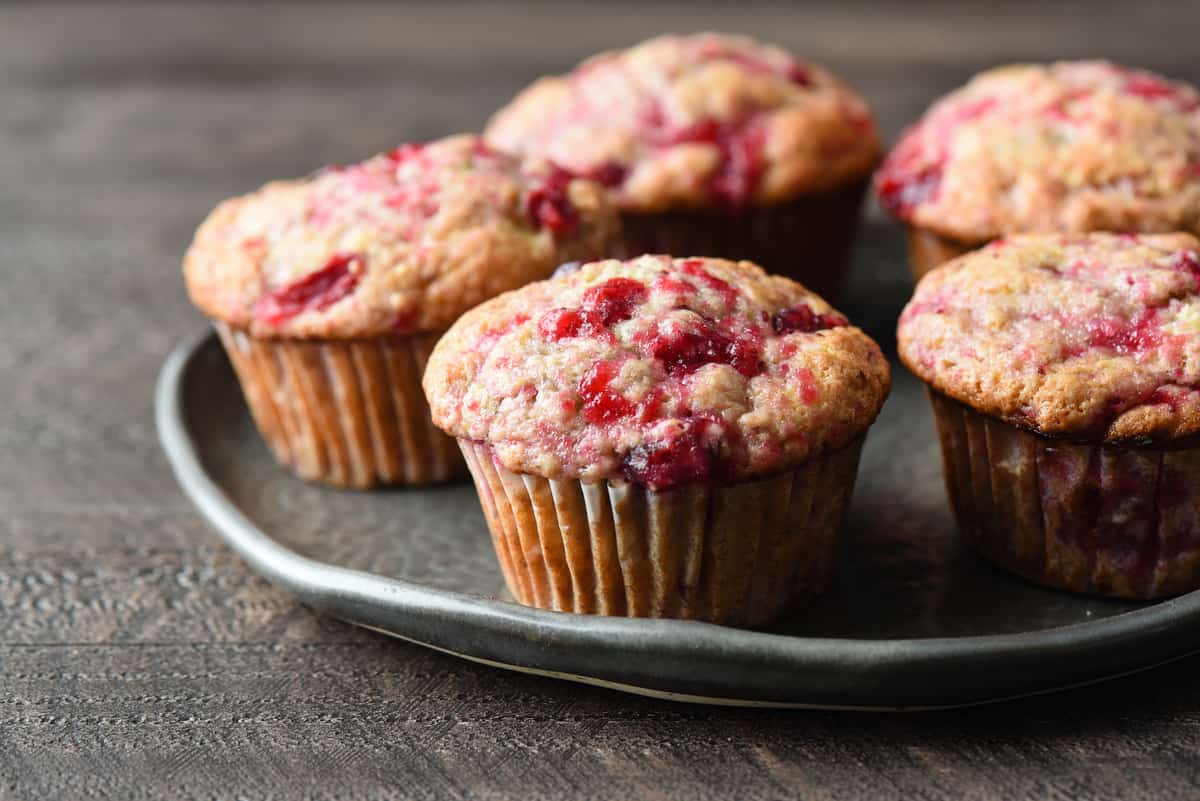 These Cranberry Sauce Muffins are the most delicious way to use up leftover cranberry sauce after Thanksgiving. You can whip these up in just a few minutes! | foxeslovelemons.com Five cranberry muffins on a gray plate.