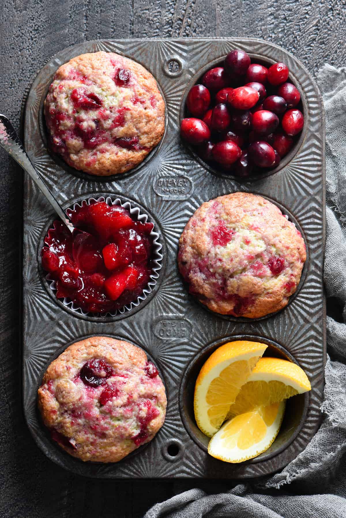 These Cranberry Sauce Muffins are the most delicious way to use up leftover cranberry sauce after Thanksgiving. You can whip these up in just a few minutes! | foxeslovelemons.com Overhead photo of muffin pan filled with three muffins, fresh cranberries, cranberry sauce and orange slices.