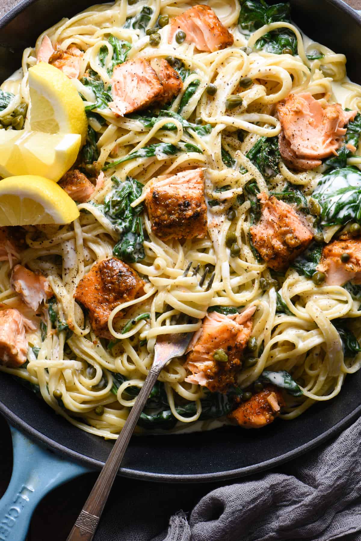 This Creamy Salmon Pasta recipe is a great way to show off what a "home chef" you are. Simple yet impressive, this is a perfect recipe for a date night at home. | foxeslovelemons.com Closeup on a fork twirling a bite of creamy salmon pasta. Spinach and capers dot the pasta dish.