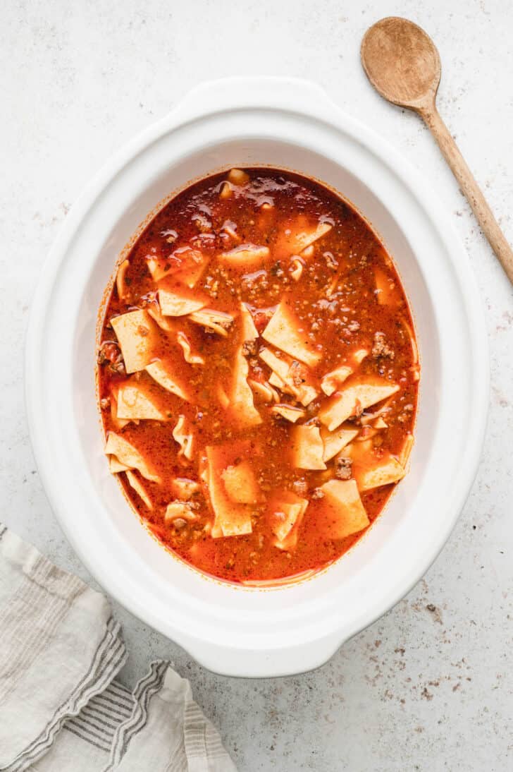 A red soup and pasta mixture in an oval white slow cooker bowl.