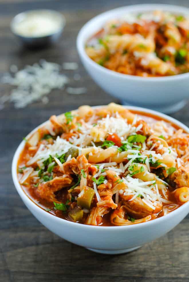 Two small white bowls filled with red soup containing pasta and chicken.