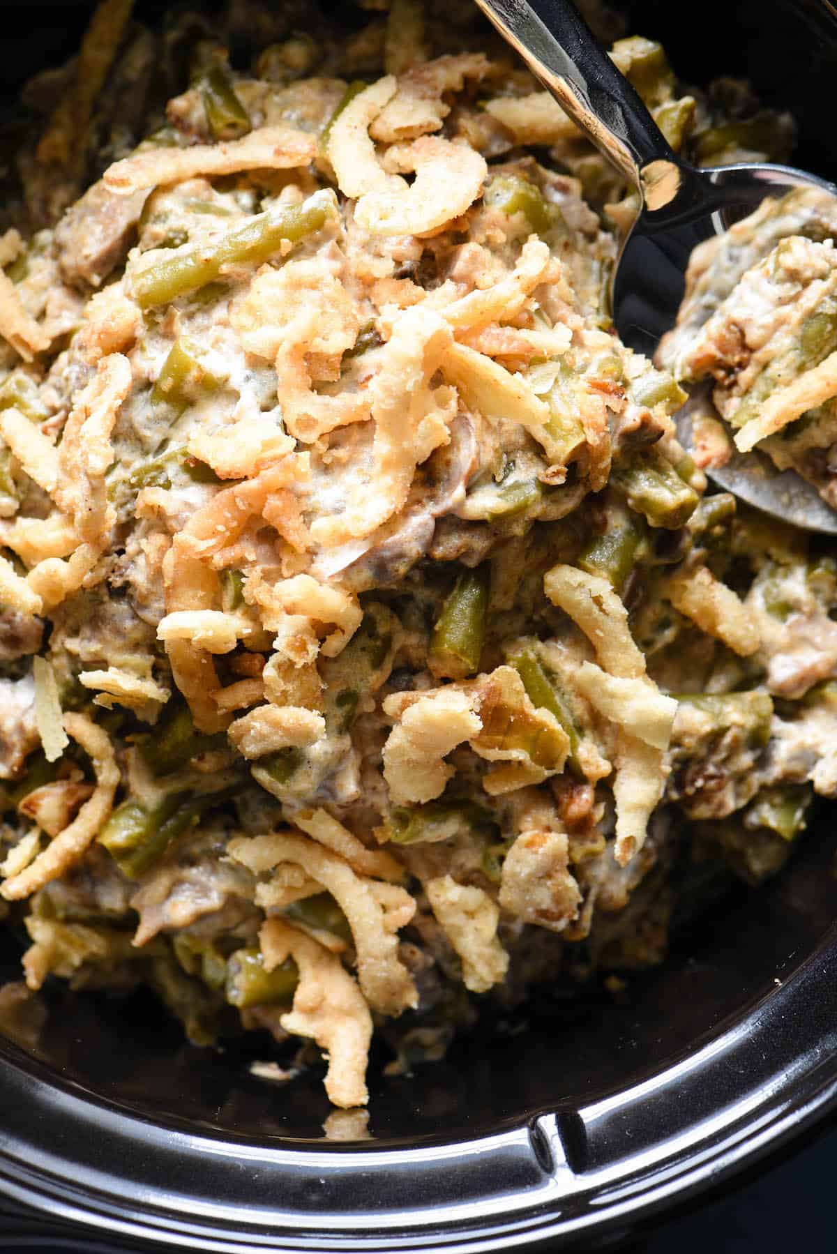 This Crockpot Green Bean Casserole is made with fresh beans and doesn't use canned soup. It's a yummy and easy upgrade to a classic dish, and doesn't take up oven space for a holiday meal! | foxeslovelemons.com A crock pot green bean casserole with a spoon digging into it.