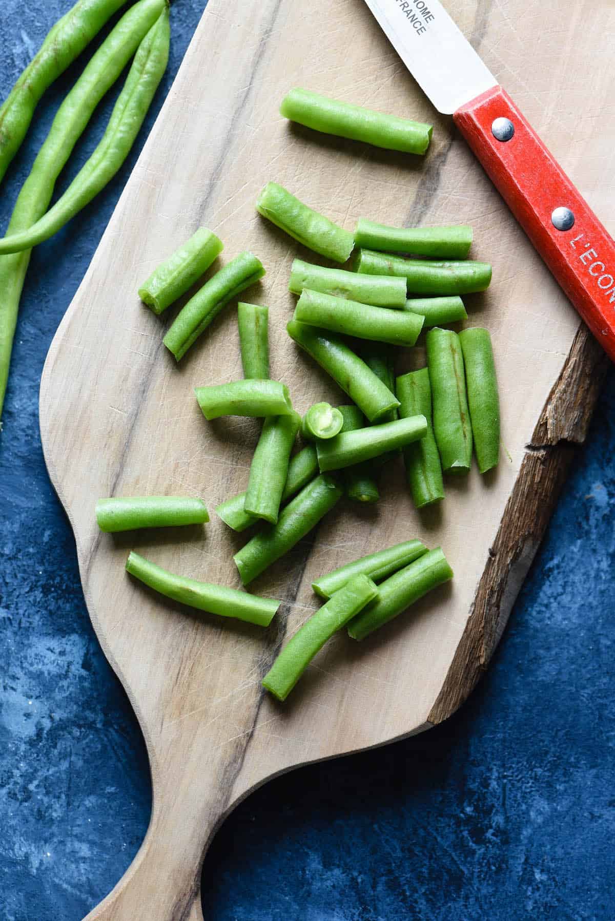 This Crockpot Green Bean Casserole is made with fresh beans and doesn't use canned soup. It's a yummy and easy upgrade to a classic dish, and doesn't take up oven space for a holiday meal! | foxeslovelemons.com A wooden cutting board and red-handled paring knife, with chopped fresh green beans.