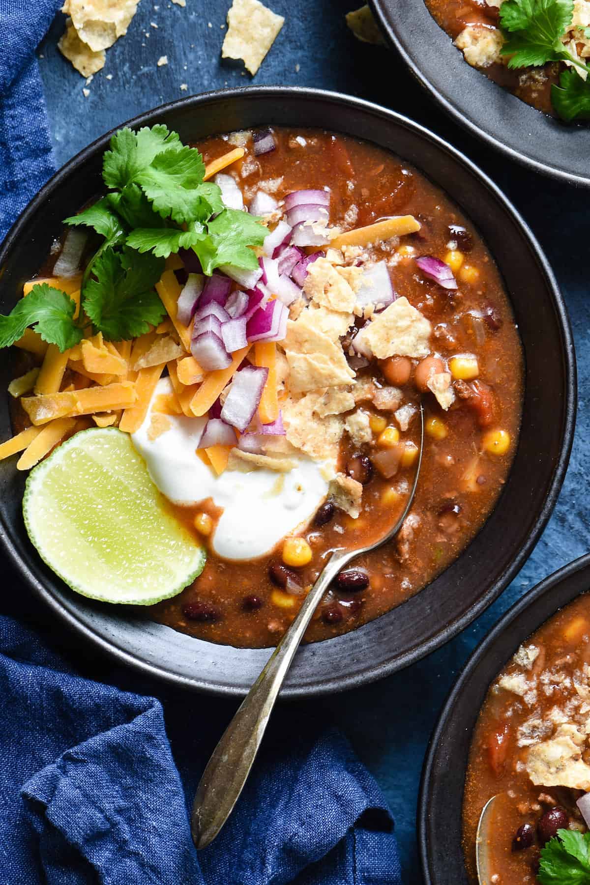 This Crockpot Taco Soup recipe comes together in just a few minutes. Includes instructions for making a large batch and freezing some for another meal, as well as a smaller batch. | foxeslovelemons.com Black bowl filled with crockpot taco soup and garnished with sour cream, lime, cilantro, cheese, red onion and crushed tortilla chips.