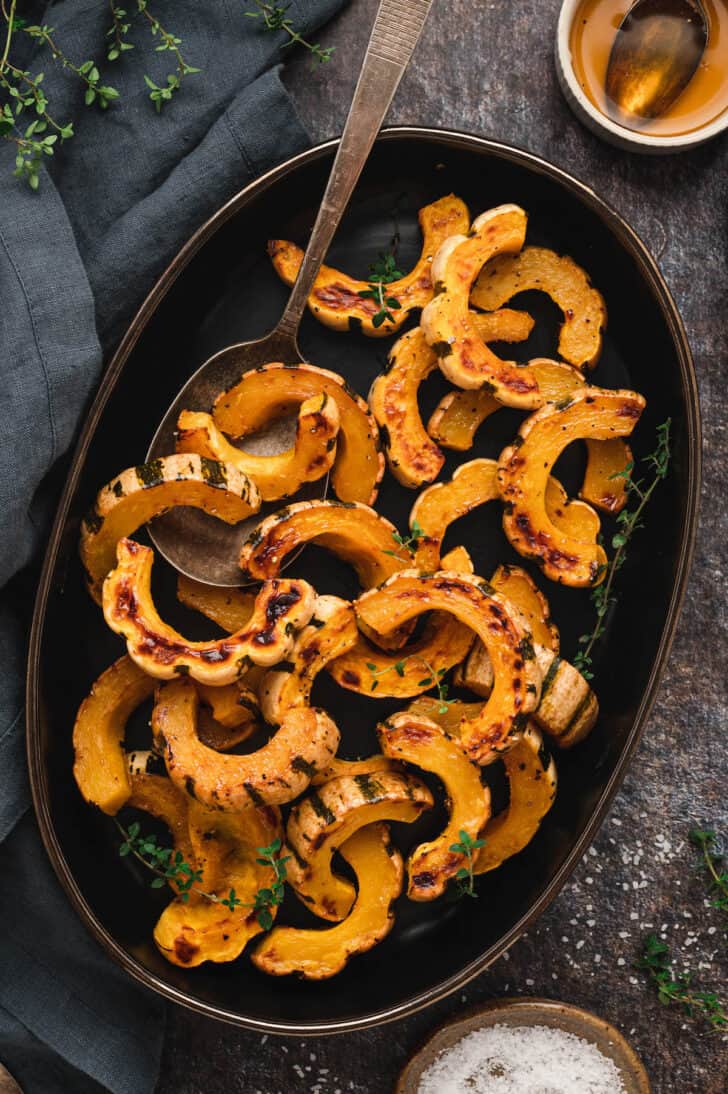 An oblong black platter topped with roasted delicata squash slices.