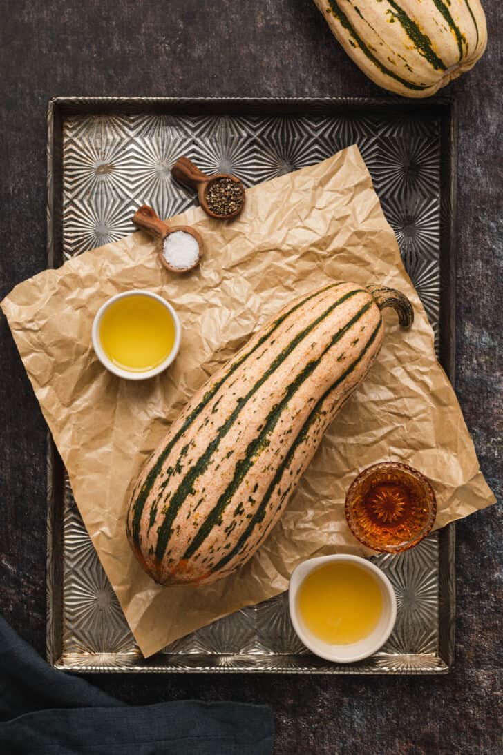 Ingredients on a textured baking pan, including a fall gourd, olive oil and spices.