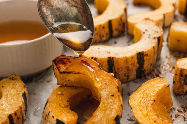 A spoon drizzling glaze over roast delicata squash slices.