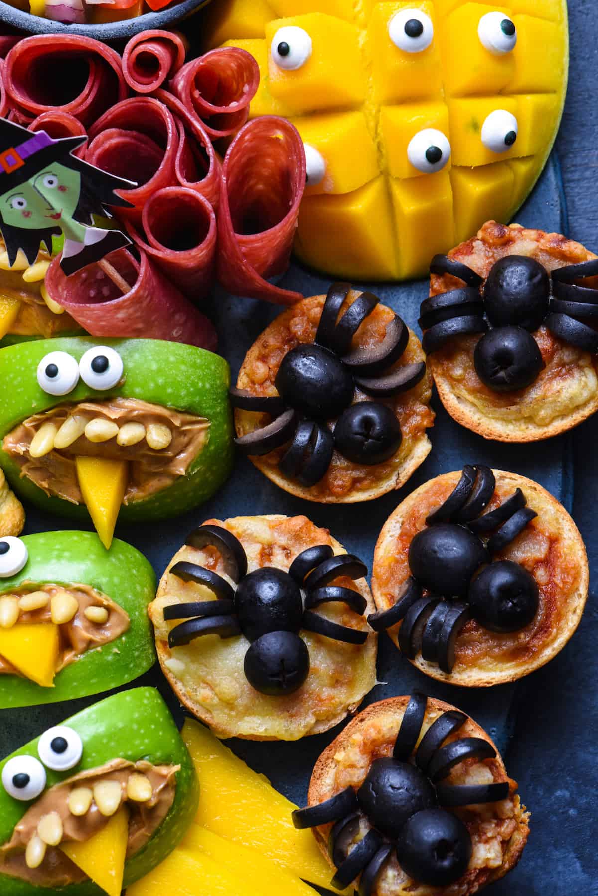 Looking for easy Halloween party food? Look no further than this simple guide to Halloween snacks. Make these edible mummies, spiders and bats for a spooky good time! | foxeslovelemons.com Closeup of Halloween food ideas, like bagel pizza bites topped with black olive "spiders"