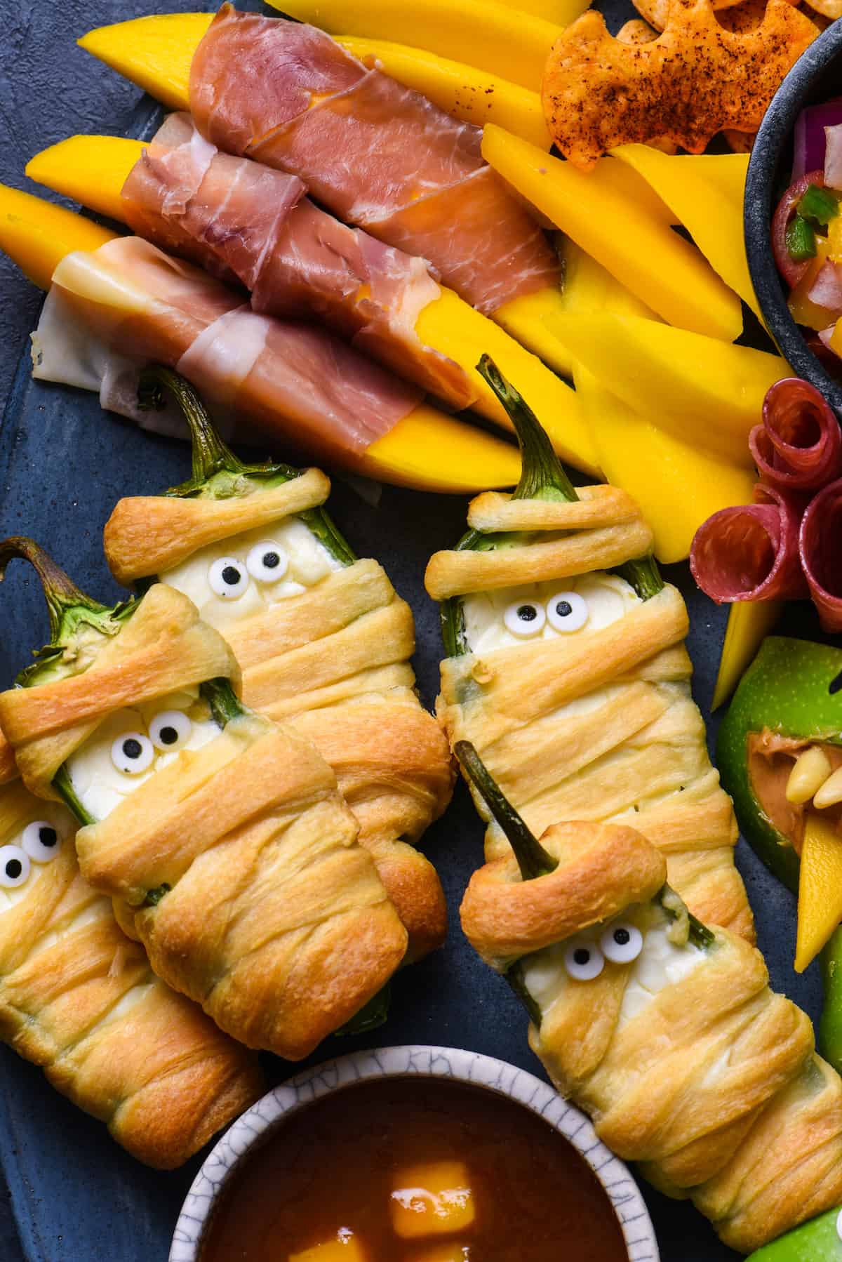 Looking for easy Halloween party food? Look no further than this simple guide to Halloween snacks. Make these edible mummies, spiders and bats for a spooky good time! | foxeslovelemons.com Closeup photo of Halloween snacks like jalapeno poppers wrapped up like mummies.