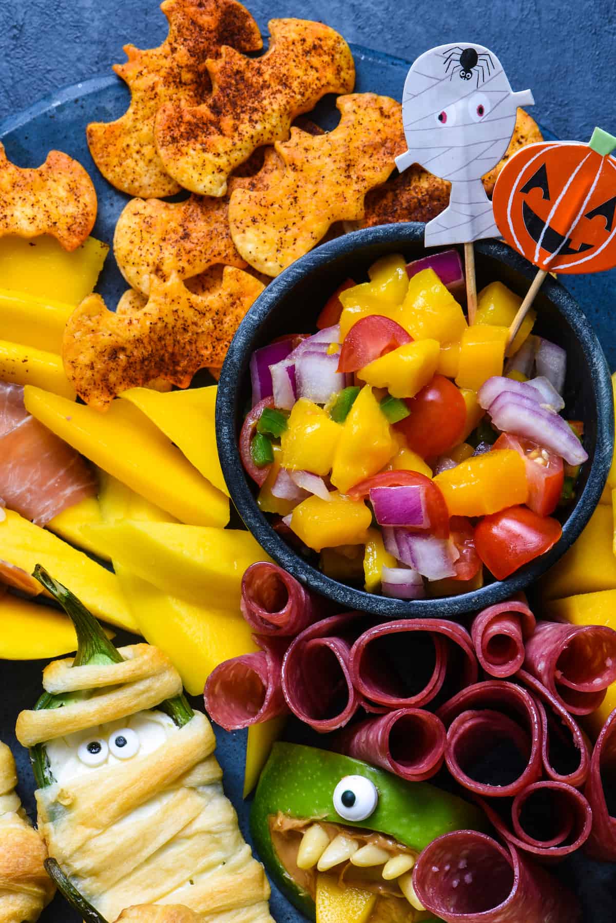 Looking for easy Halloween party food? Look no further than this simple guide to Halloween snacks. Make these edible mummies, spiders and bats for a spooky good time! | foxeslovelemons.com Closeup of small bowl of chopped mango salsa with tortilla chip "bats"