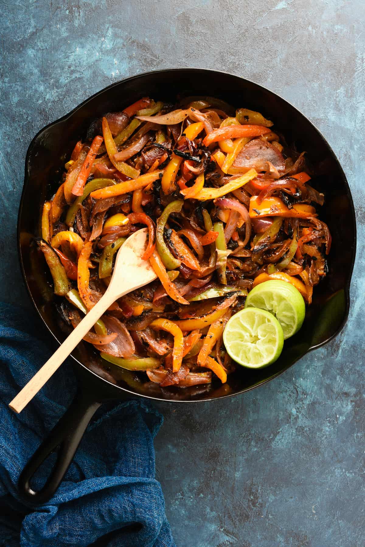 These Fajita Veggies have the restaurant flavor you love, made at home without a seasoning packet. Use them for vegetarian fajitas, or add steak, chicken or shrimp to the mix! | foxeslovelemons.com Cast iron skillet filled with cooked fajitas veggies, with wooden spoon and lime halves.