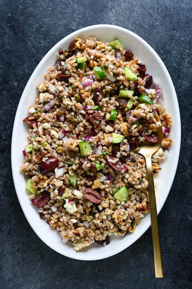 The best ever farro salad on a white platter with a gold serving spoon digging in.