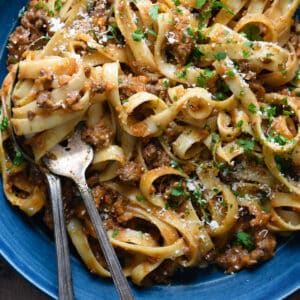 A blue ceramic bowl filled with fettuccine bolognese, with a fork twirling the pasta.