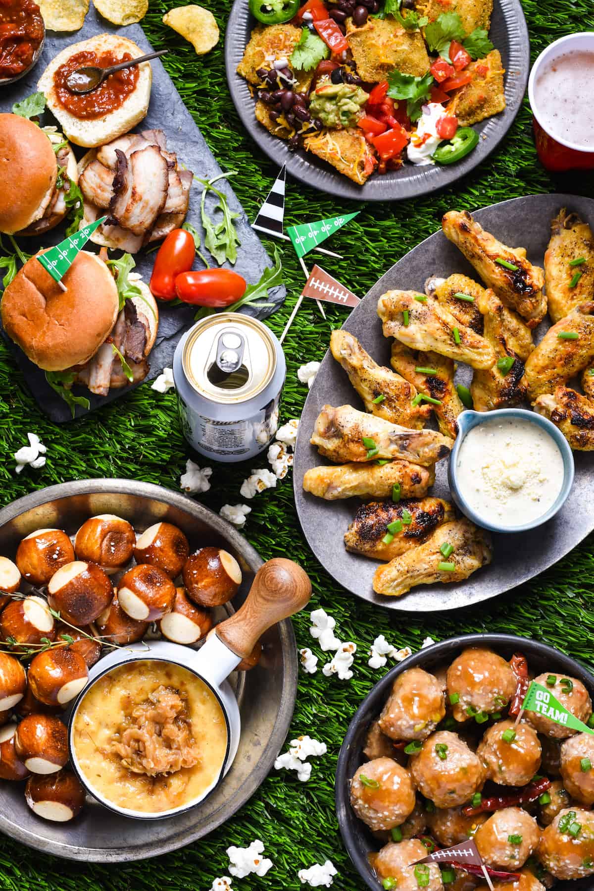 Epic Game Day - A flavor-packed, chef-inspired game day feast that YOU can make at home! | foxeslovelemons.com Astroturf topped with various types of tailgating food, including sliders, nachos, chicken wings cheese dip and meatballs.