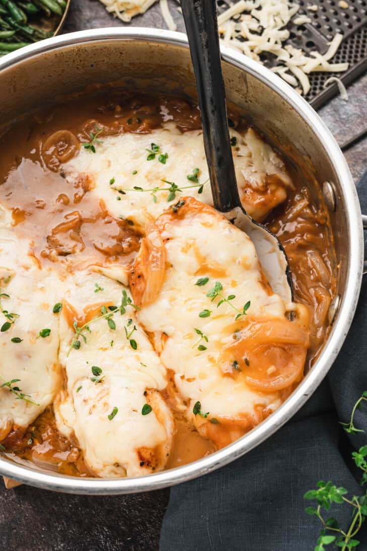 French Onion Skillet Chicken with a black spoon lifting one piece of chicken out of the skillet.