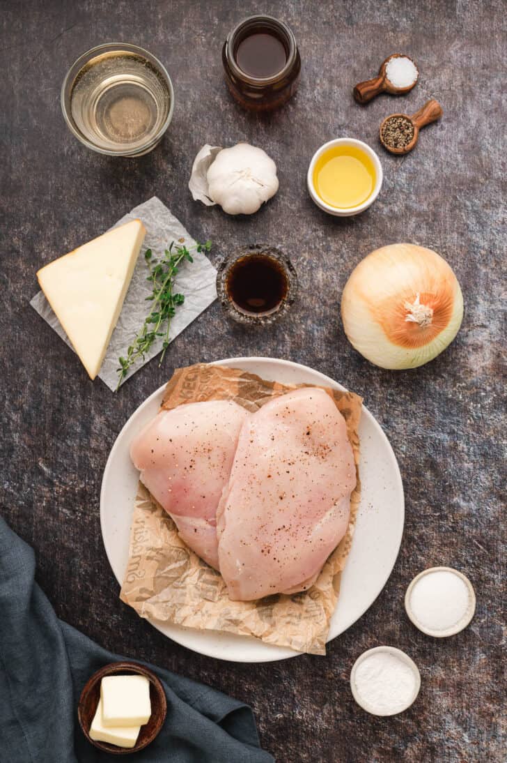 Ingredients laid out on a dark surface, including poultry, onion, garlic, herbs, cheese and spices.