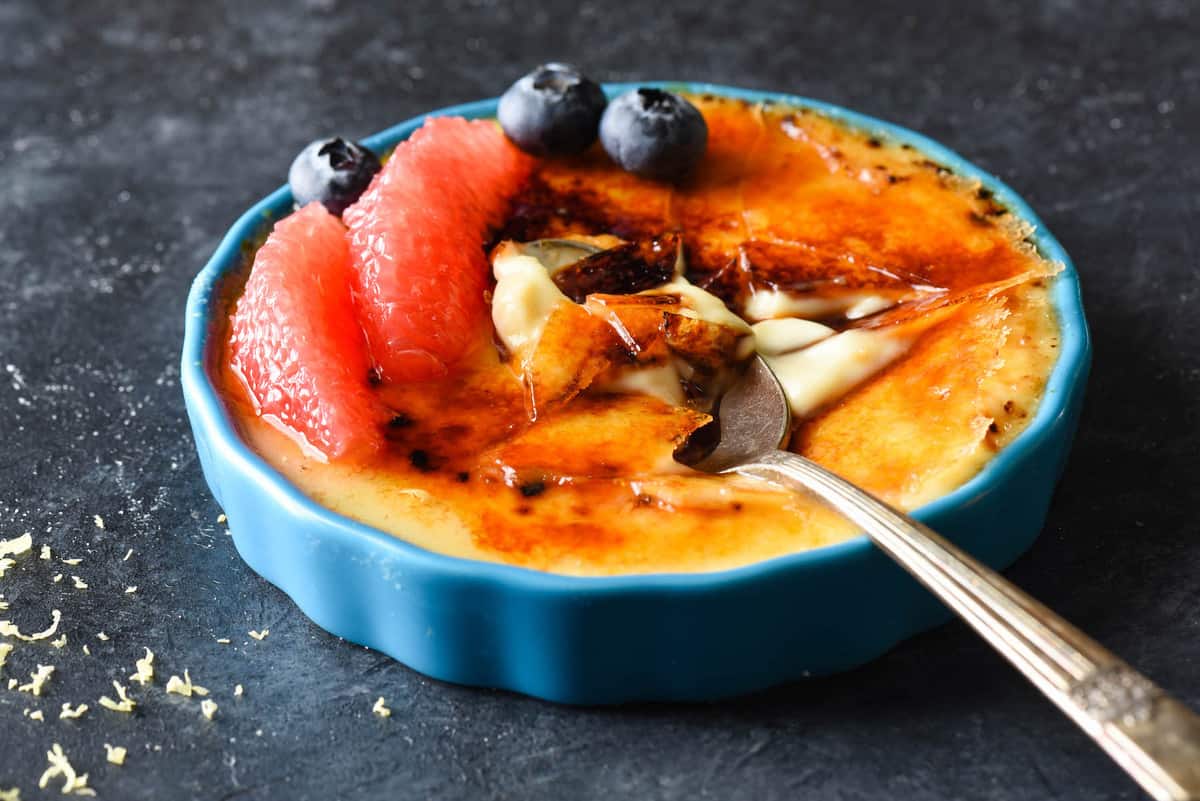 Preparing, torching and serving this Grapefruit Crème Brûlée is bound to make you feel like the kitchen superstar you are. Rich custard is flavored with sweet grapefruit juice and zest for a refreshing twist on a classic dessert. | foxeslovelemons.com A blue ramekin of custard with crunchy torched sugar on top, with a spoon digging into it. Grapefruit segments and blueberries garnish the custard.