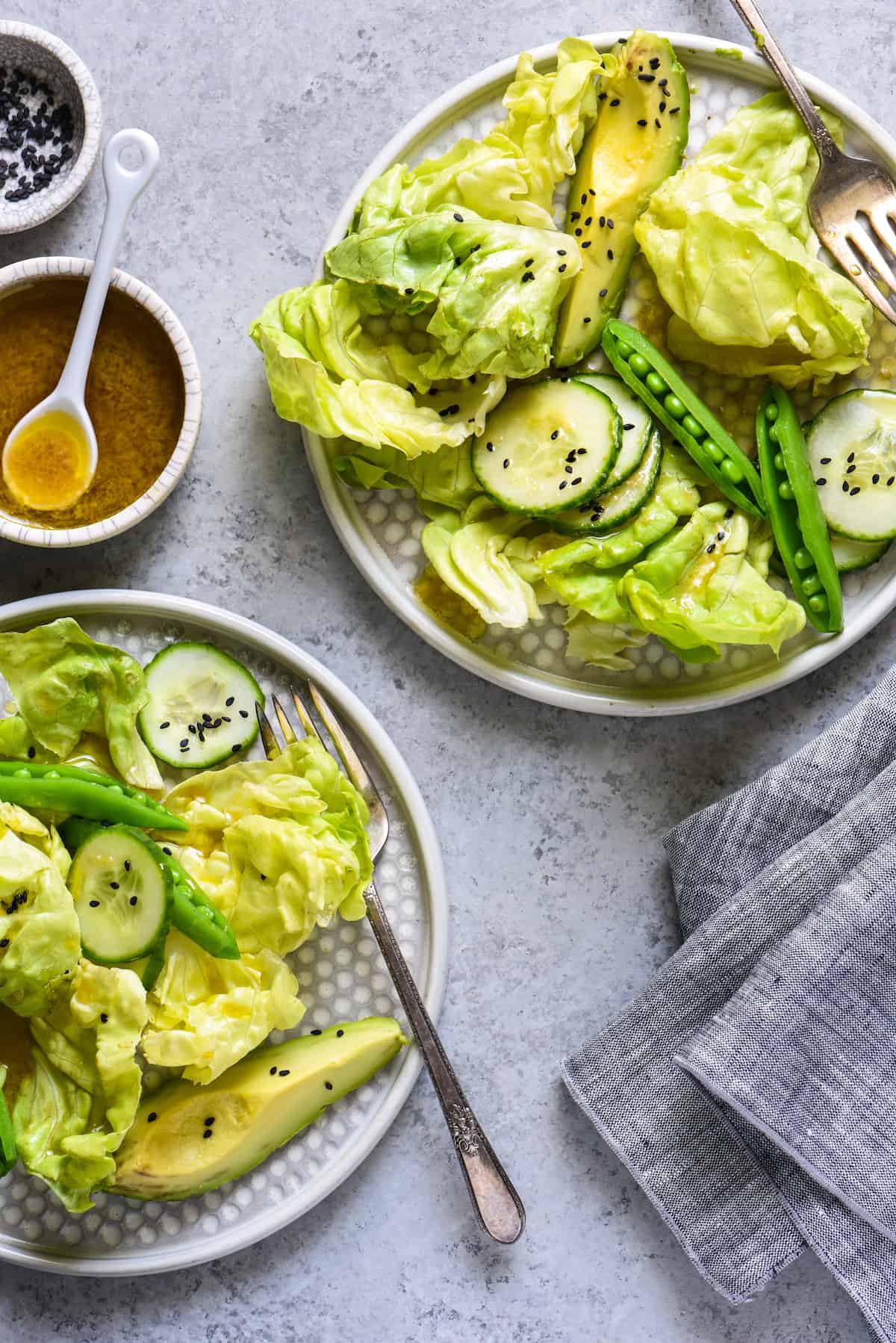 Two plates of green salad with a small bowl of miso dressing nearby.