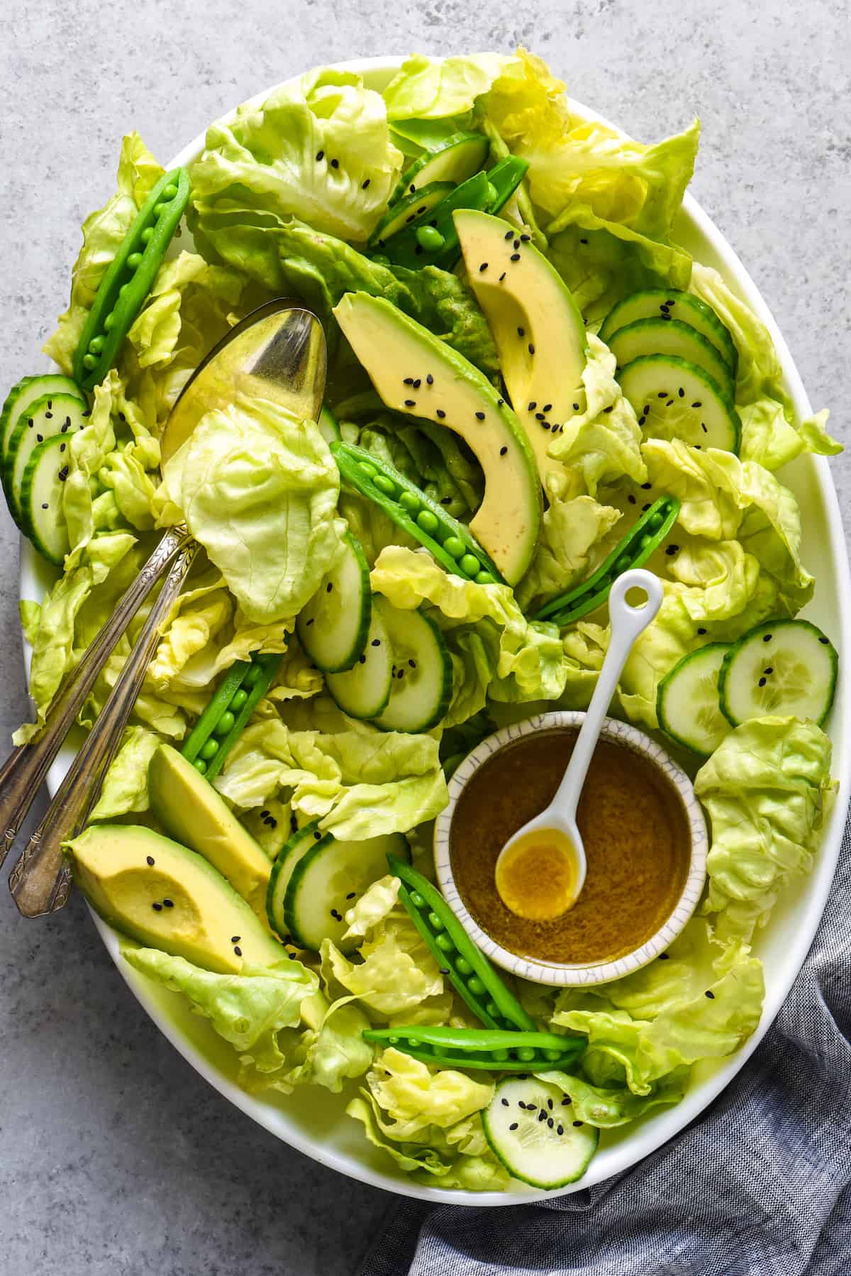 This Miso Dressing Recipe will turn any typical bowl of greens into a showstopping salad that will become the star of your meal! | foxeslovelemons.com Large platter of green salad with lettuce, avocado, cucumber and peas, and a small bowl of brown salad dressing.